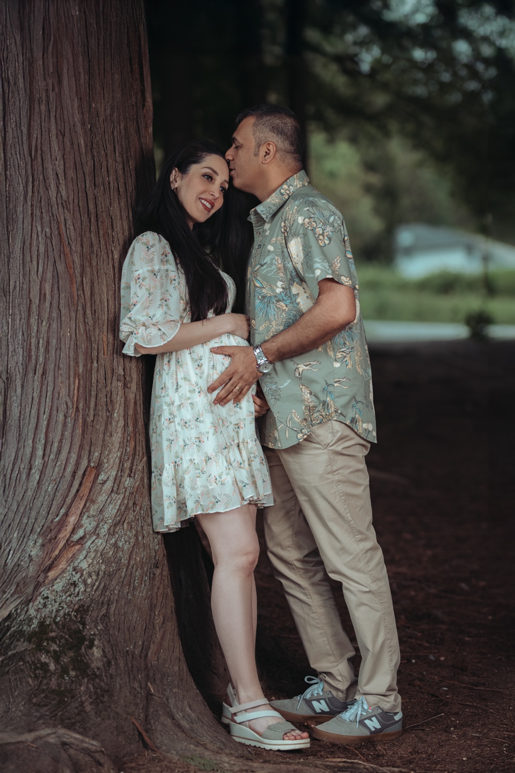 Father kissing the mother’s forehead during a woodland maternity portrait